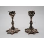 A pair of cast white metal continental silver candlesticks, with scrolling foliate roundel bases,