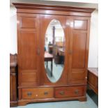 An Edwardian mahogany wardrobe with shaped cornice over central mirrored door flanked by panel doors