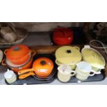 A collection of Le Crueset orange and yellow kitchenware including lidded pots, frying pans etc