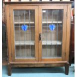 An early 20th century oak arts and crafts style glazed bookcase with pair of leaded glass doors