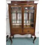 A 20th century mahogany display cabinet with pair of bevelled glass doors over pair of drawers on