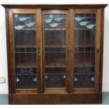 An early 20th century mahogany bookcase with three leaded stained glass sliding doors on plinth