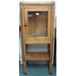 An early 20th century pine glazed peer cabinet with single glazed door on shaped square supports