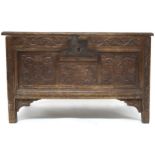 A 17TH/18TH CENTURY OAK CARVED PANELLED COFFER with panel hinged lid over panelled front carved with