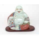 A CHINESE MODEL OF BUDDHA  seated with rosary beads and patterned costume, on a wooden stand,