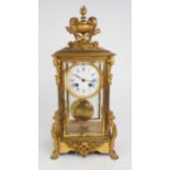 A FRENCH GILDED BRASS AND GLASS TIMEPIECE of tall rectangular form, the top with flaming urn and