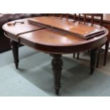 A Victorian mahogany oval wind out extending dining table with two spare leaves on turned