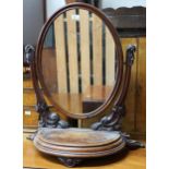 A Victorian walnut dressing mirror with oval pane suspended on carved arms on half moon base