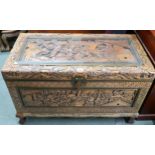 A 20th century Chinese camphorwood blanket chest carved with village scenes on shaped feet joined by