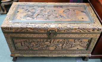 A 20th century Chinese camphorwood blanket chest carved with village scenes on shaped feet joined by