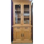 A contemporary pine bookcase with moulded cornice over pair of glazed doors on base with two short
