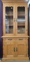 A contemporary pine bookcase with moulded cornice over pair of glazed doors on base with two short