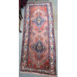 A red ground tribal Hamadan runner with two geometric medallions and multicoloured borders, 232cm