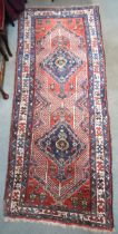 A red ground tribal Hamadan runner with two geometric medallions and multicoloured borders, 232cm