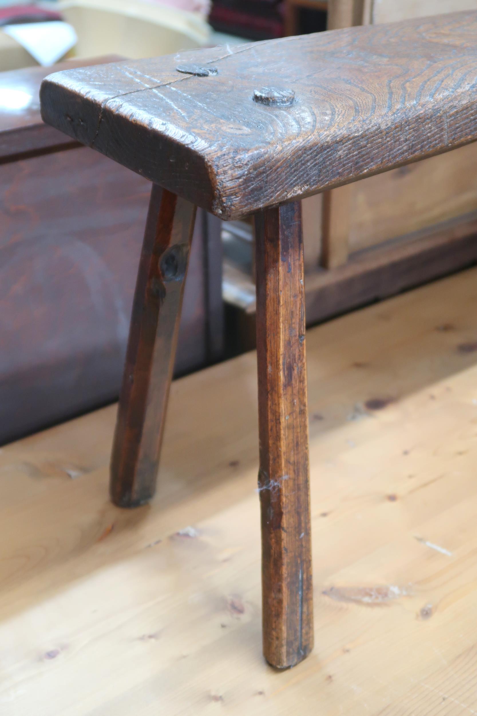 A 19th century elm bench stool with plank seat on chamfered splayed supports, 40cm high x 88cm - Image 2 of 2