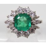 AN EMERALD & DIAMOND CLUSTER RING set with a step cut emerald of approx 8.95mm x 8.33mm x 4.6mm in