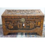A 20th century Chinese camphorwood blanket chest, carved with village scenes on shaped feet, 59cm
