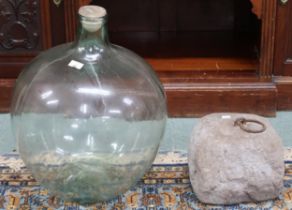 A lot comprising a 19th century animal tether stone with inset iron ring and a glass demijohn (2)