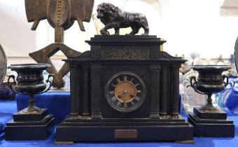 A slate mantle clock with spelter Medici lion finial with a pair of urn shaped garnitures
