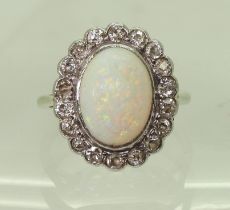 A WHITE OPAL & DIAMOND CLUSTER RING mounted in white metal , set with a central oval cabochon