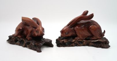 A PAIR OF CHINESE CARVED WOOD HARES  each recumbent on pierced foliate and rocky bases, glass
