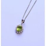A 9ct white gold peridot and diamond oval cluster pendant