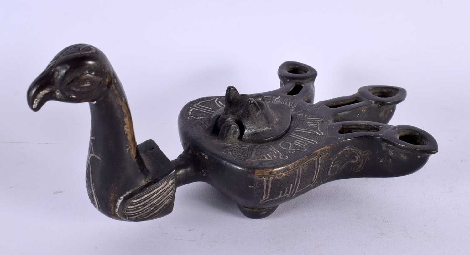 A 19TH CENTURY MIDDLE EASTERN SILVER INLAID BRONZE OIL LAMP formed as a bird, decorated with motifs.