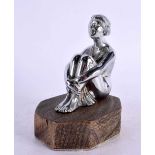 AN ART DECO CHROME CAR MASCOT formed as a seated female clutching her legs. 14 cm x 9 cm.