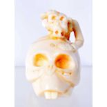 A CARVED BONE NETSUKE IN THE FORM OF A SKULL SURMOUNTED WITH A SKELETAL CREATURE. 5.2cm x 3.3cm x