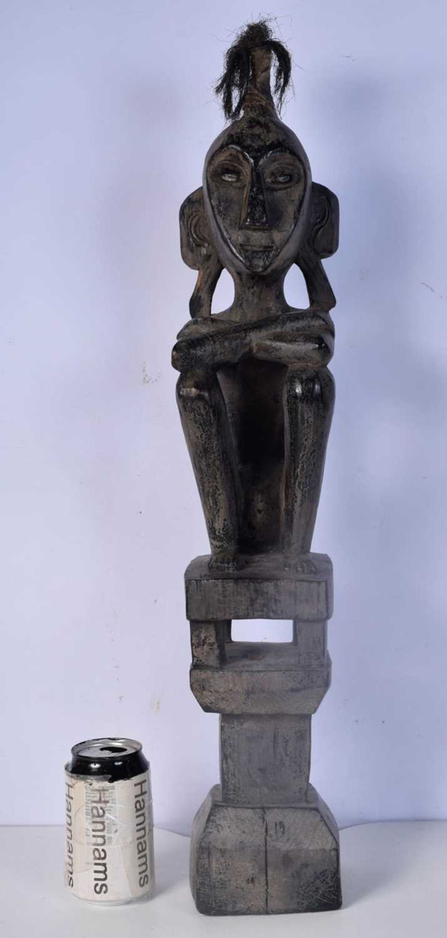 A carved wooden headhunter/ancestor figure from the Leti Islands (Indonesia), seated on a house