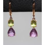 A PAIR OF DROP EARRINGS, each claw set with an oval facet cut peridot and tear cut amethyst to plain