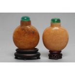 TWO SIMILAR CHINESE SNUFF BOTTLES, one in pale honey serpentine, the other in amber coloured