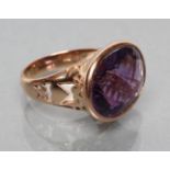 AN AMETHYST RING, the oval slightly domed stone with all-over facet cutting, collet set to open