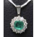 AN EMERALD AND DIAMOND CLUSTER PENDANT, the circular facet cut emerald claw set to a border of