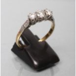 A THREE STONE DIAMOND RING, the old brilliant cut stones claw set to white shoulders and a plain