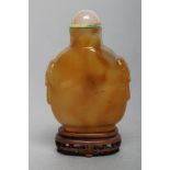 A CHINESE HONEY AGATE SNUFF BOTTLE with grey and amber cloud effect, carved in relief with two