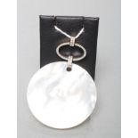 A MOTHER OF PEARL POLISHED CIRCULAR PENDANT hung from a diamond set open oval panel on similar set