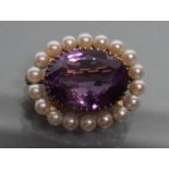 AN AMETHYST AND PEARL BROOCH, the oval facet cut amethyst claw set to a border of peg set cultured