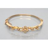AN EDWARDIAN STIFF HINGED BANGLE, the upper section with open scrolls and seed pearl set