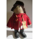 A Paddington Bear, with amber eyes, brown felt hat, red felt coat, black wellies and original label,