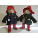 Two Paddington Bears, both in red Dunlop boots and red hats, one in a blue coat and one in green,