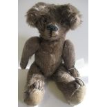 An old teddy bear, with light brown plush, glass eyes, sewn nose, large ears, hump and fabric