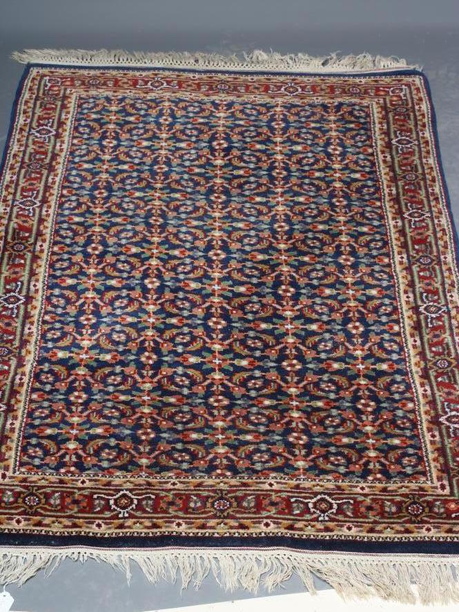 A PERSIAN RUG, the navy blue field with repeating pattern of foliate scrolls and flower heads, the