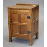 A ROBERT THOMPSON ADZED OAK BEDSIDE CABINET of canted multi-panelled oblong form, the moulded
