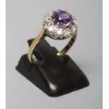 AN AMETHYST AND DIAMOND CLUSTER RING, the circular facet cut amethyst claw set to a border