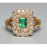 AN EMERALD AND DIAMOND CLUSTER DRESS RING, the oblong facet cut emerald claw set to a double