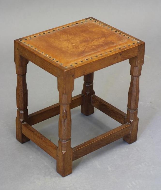 A ROBERT THOMPSON ADZED OAK STOOL of oblong form with padded cow hide seat, on faceted turned and