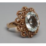 AN AQUAMARINE COCKTAIL RING, the oval facet cut stone claw set to a rope twist open border and plain