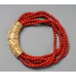A SIX STRAND CORAL BEAD BRACELET, the strands set into a crescent shaped panel clasp chased with