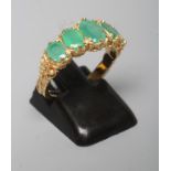 A FIVE STONE EMERALD RING, the graduated oval facet cut stones in claw and rub-over settings to leaf